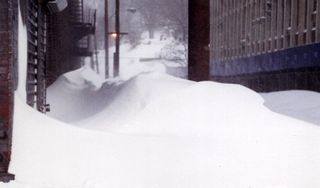 Die Abbildung zeigt tiefen Schnee und Schneeverwehungen zwischen zwei Stadthäusern.