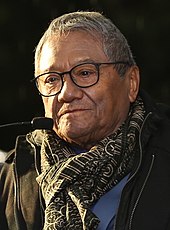 A man wearing glasses, a black jacket and a scarf.
