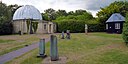 ☎∈ Some observatory buildings at the Institute of Astronomy of the University of Cambridge. The Northumberland Telescope is in the dome on the left. The covered structures in the foreground are mounts for portable telescopes.