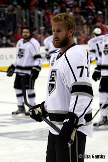 Photographie d'un joueur de hockey avec un maillot blanc, de la barbe et pas de casque