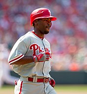 A man in a grey baseball uniform and wearing a red helmet faces right