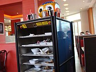 A mobile cupboard filled with trays with many dirty dishes driving through a restaurant.