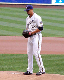Seorang pria di putih seragam bisbol dan angkatan laut topi berdiri di atas gundukan pitcher