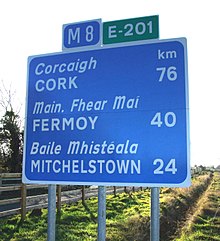 Route numbers displayed on top of a route confirmation sign in Ireland M8 cropped wiki route confirmationBE.JPG