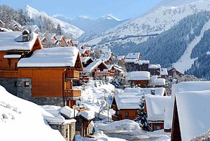 Snow covered wooden chalets with mountains in the background.
