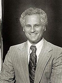 Black-and-white photo of a man with a wide smile and short curly hair wearing a light-colored suit