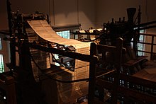 A picture of a wooden looming machine with a long chain of punched cards looping through it.