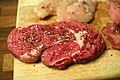 Würzen eines Steaks vor dem Braten mit grobem Salz und schwarzem Pfeffer