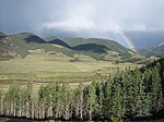 Un pequeño río serpentea a través de montañas bajo un arco iris.