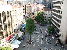 Birkaç kat yüksekten bakılan, yaya olarak insanların ve dükkan işaretlerinin bulunduğu nispeten yoğun bir cadde.