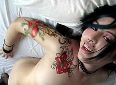 Sublime Dream (Suicide Girls). La position apparemment dominante du photographe permet de montrer à la fois le visage, les tatouages et piercings, tout en suggérant discrètement la nudité de la jeune femme.