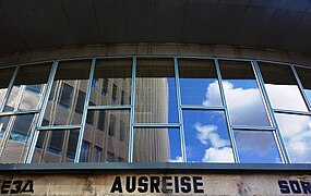 'Ausreise' staat boven de ingang, met hoogbouw Spreedreieck in de weerspiegeling van het glas (2019).
