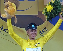 Seorang pria yang mengenakan jersey kuning dengan tangannya tinggi-tinggi.