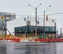 Photo of a light rail and subway station entrance under construction. White cladding panels have been affixed to a small portion of the exterior.