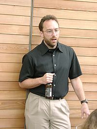 Jimmy Wales leaning on a fence and holding a bottle