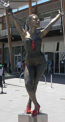 काइली की एक कांस्य प्रतिमा सितारे के आकार के एक मूर्तितल के ऊपर रखा गया है, जिसमें उन्हें एक नृत्य मुद्रा में दिखाया गया है। उनके पैर आर-पार हैं तथा वे अपने दोनों हाथों को अपने सर के ऊपर फैलाते हुए अपनी कमर से झुकी हुई हैं। यह प्रतिमा शीशे के एक आधुनिक इमारत के सामने एक सार्वजनिक चौराहे पर खड़ी है, जहां बहुत से लोगों की आवाजाही है।