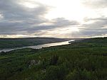 Tramonto su un fiume che si snoda attraverso fitte foreste sempreverdi.