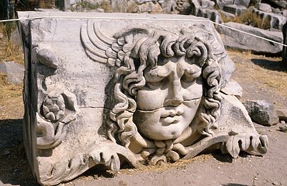 Sculpture en ronde bosse du masque de Méduse, présentant un visage idéalisé aux traits réguliers, une abondante chevelure et des ailes en arrière de la tête.