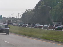 A six-lane freeway with wooded surroundings and a traffic jam