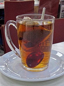 a glass mug on a china saucer, of tea without milk, with a tea bag and a spoon visible in it