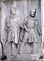 Парфянин (справа) во фригийском колпаке, изображённый как военнопленный в цепях, который держит римлянин (слева); Триумфальная арка Септимия Севера, Рим, 203 г. н. э.