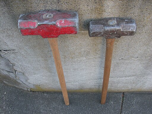 Two sledgehammers standing on end and leaning against a wall