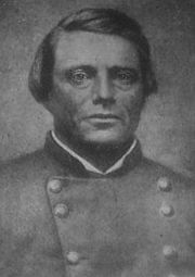 Black and white photo shows a clean-shaven man with dark hair. He wears a gray military uniform.