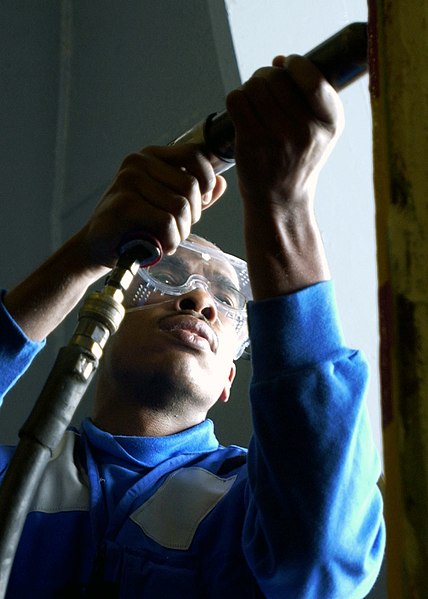 File:US Navy 071210-N-7571S-010 Aviation Boatswain's Mate Airman Rashad Gloster uses a needle guns to chip away paint from a hangar bay elevator door in preparation for painting.jpg