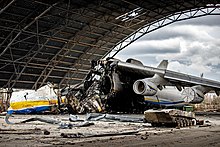 Vrak zničeného lietadla pod strechou poškodeného hangára