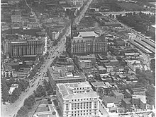 Federal Triangle area facing east in 1923. Pennsylvania Avenue is in the left, the District Building is in the foreground and the Post Office Building and Center Market are in the background. Aerial Photograph of Pennsylvania Avenue in Washington, DC including the District Building and the Post Office Building, 1923.jpg