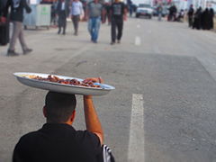 Un homme tenant une assiette pleine de dattes sur sa tête pour passer les pèlerins d'Arba'een