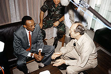 Overhead view of Kagame and Perry seated on leather seats with a large microphone visible and another army member in the background
