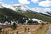 Diversi piccoli edifici in legno in una valle con sempreverdi e montagne innevate in lontananza