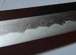 A Japanese katana made of laminated steel. The outer skin is forged from alternating layers of steel with differing carbon content, and folded upon itself many times, producing a mokume (wood-eye) pattern. Katana - showing alternating layers.jpg