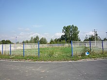 На фотографии изображена кольцевая развязка, частично окруженная белыми воротами и заросшая сорняками, в центре которой - материализованное устье второй ямы Маркиенн, открытой Компанией каноньер-де-Лилль.