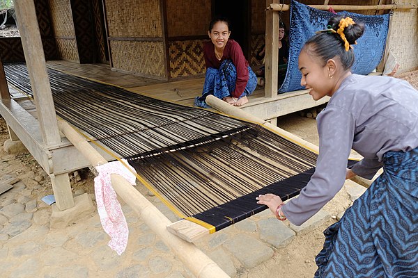 Wrapping the warp threads around the warp beam of a loom in preparation for weaving.