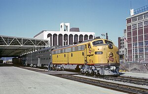 A yellow Milwaukee Road EMD E9 hauling two stainless steel bilevel coach cars