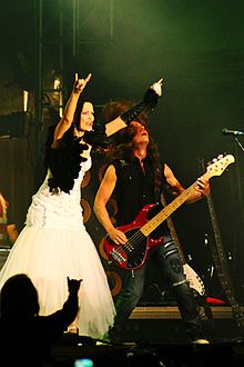 Une femme brune habillée d'une robe blanche et noir et un homme jouant de la guitare