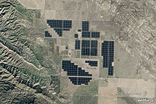 Een satellietbeeld van wat lijkt op semi-regelmatig uit elkaar geplaatste delen van zwarte tegels in een vlakte, omringd door landbouwgrond en graslanden