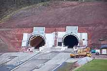 Twin tunnel entrance in hillside. A short, grey arch bridge is in the upper right background.