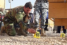 Al Asad Air Base, Iraq: An Iraqi Police officer in the Basic Criminal Investigation Course here lays down numbered tabs on a mock crime scene to mark evidence during the class' final exercise. USMC-18810.jpg