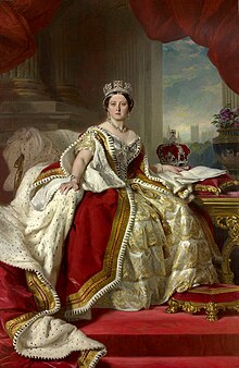 Queen Victoria in coronation garb. Her left hand rests on a table beside a crown. The Houses of Parliament are visible outside a window.