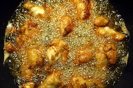 Chicken wings being fried in a pan filled with corn oil