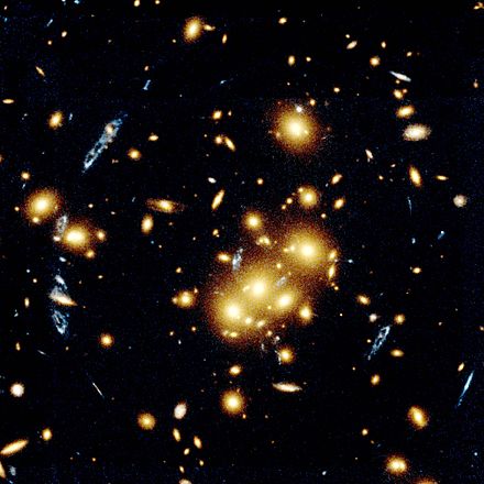 This image shows several blue, loop-shaped objects that are multiple images of the same galaxy, duplicated by the gravitational lens effect of the cluster of yellow galaxies near the middle of the photograph. The lens is produced by the cluster's gravitational field that bends light to magnify and distort the image of a more distant object.
