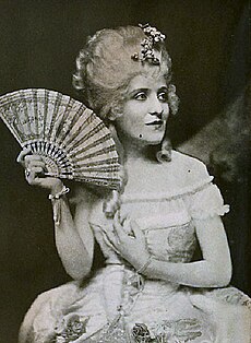 Black and white photo of a white woman in a wig with a fan.