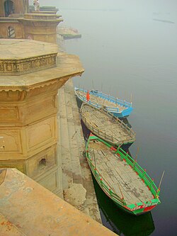 Three boats parked near steps of a ghat built in yellow stones.