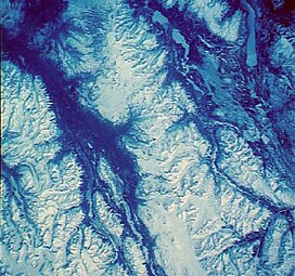 An overhead view of snow-covered mountains with intervening river valleys.