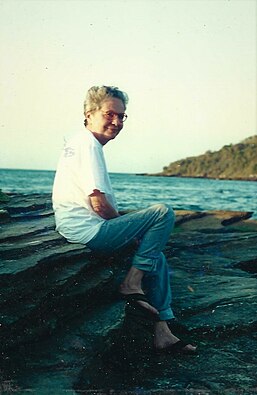 Maria Helena Dutra sentada em pedras a frente ao mar.