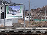 旧駅のホーム駅名標と、右奥に見える新駅舎（2016年1月）