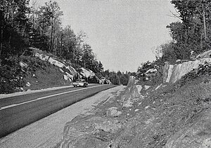 Black and white image of a paved highway travelling through a rock cut